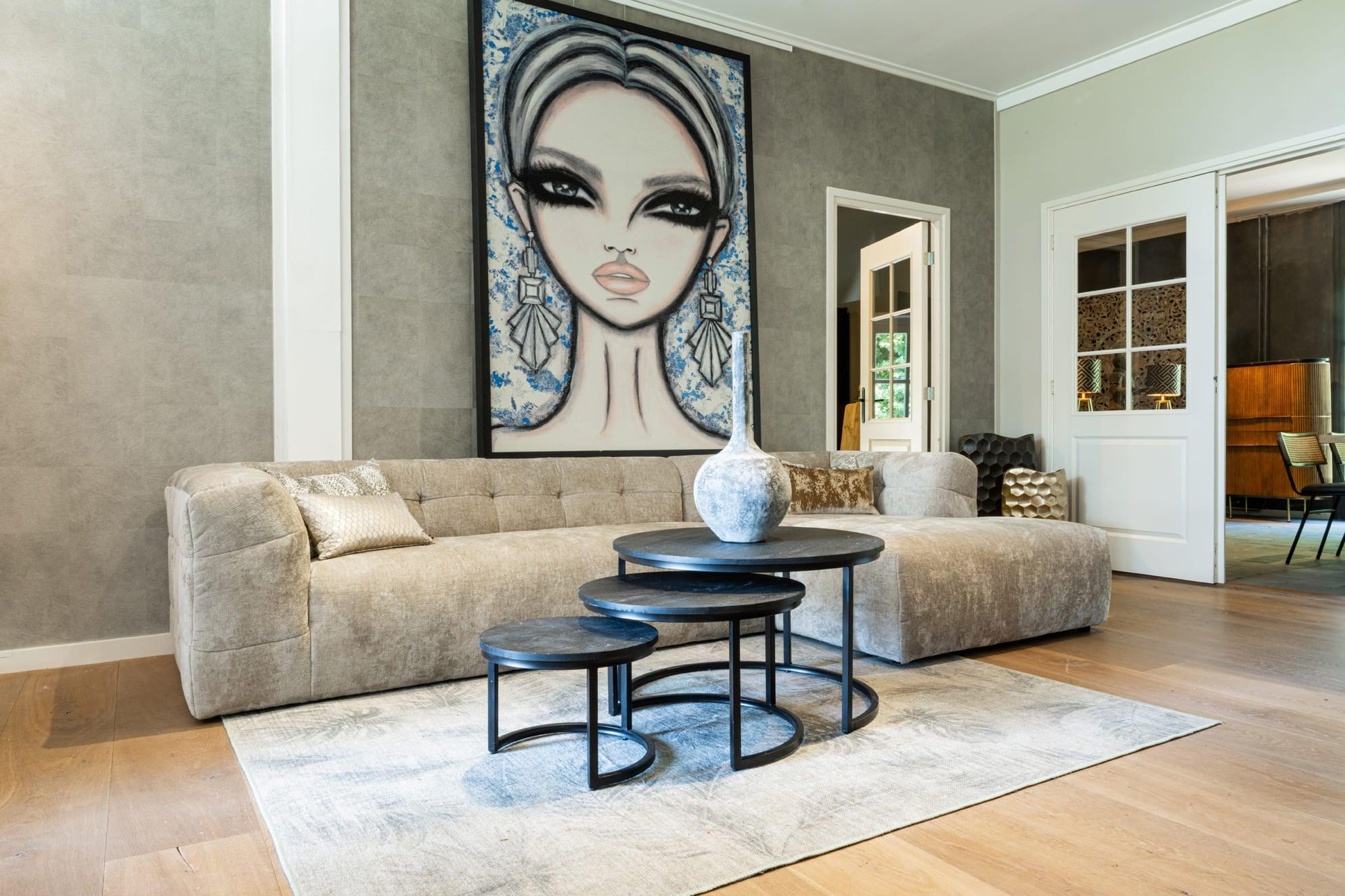 "Elegante beige hoekbank in een chique woonkamer met stijlvolle kunst, ronde zwarte salontafels en een vintage piano, omgeven door zachte aardetinten en luxe texturen."