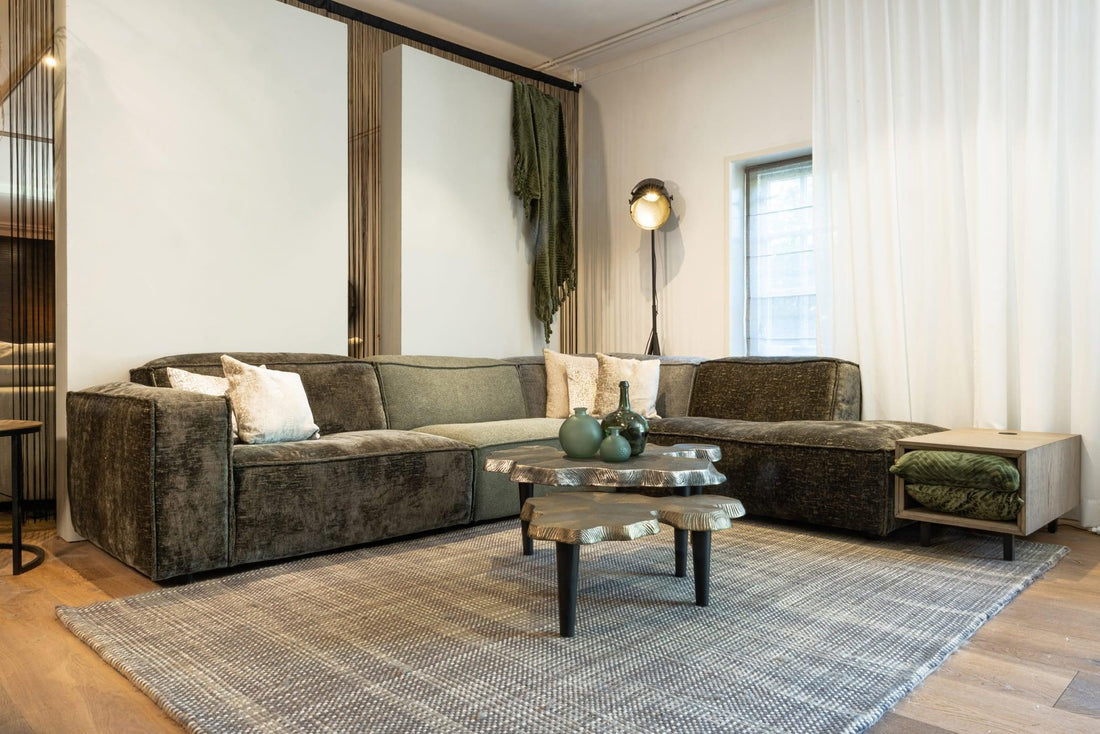 "Stijlvolle woonkamer met fluwelen hoekbank, houten salontafel met organische vorm, moderne staande lamp en elegante witte gordijnen."