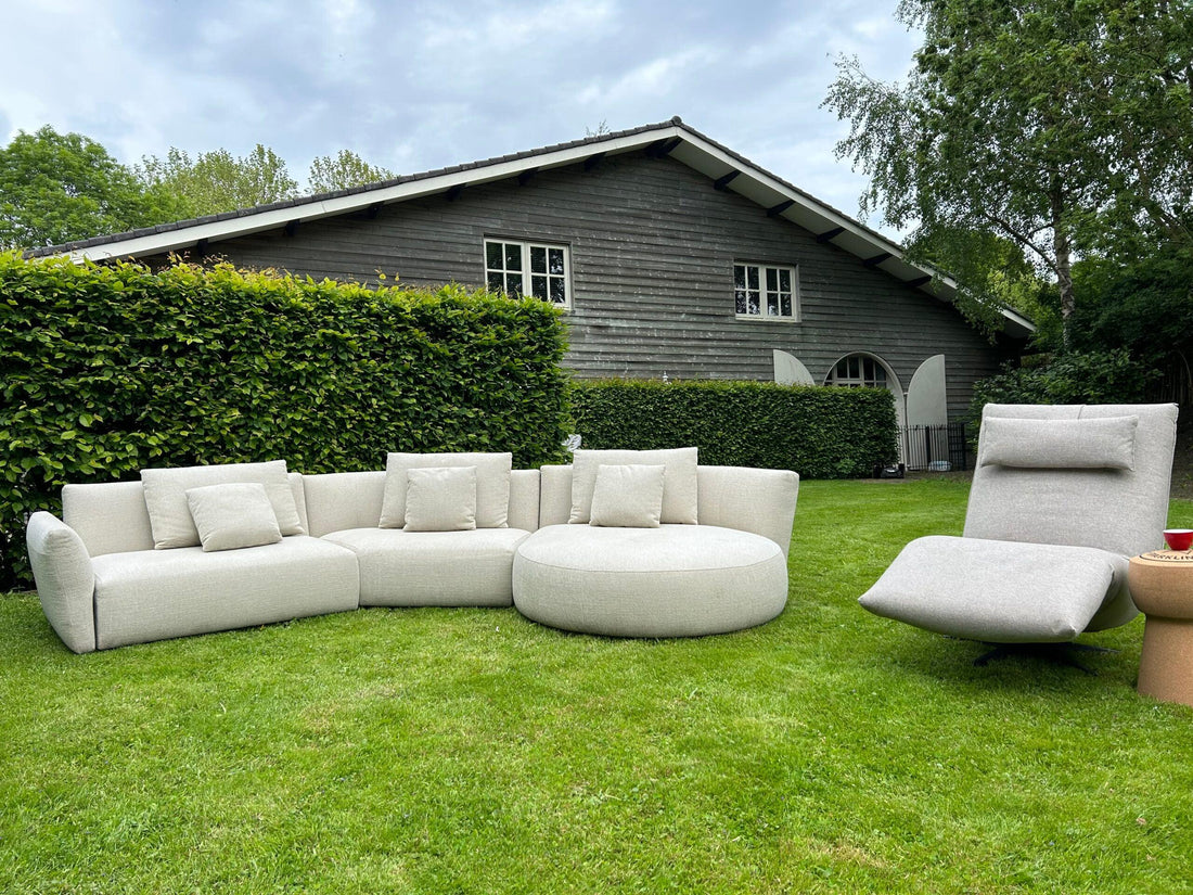 "Design tuinmeubelset bestaande uit een modulaire loungebank en relaxfauteuil op een weelderig groen gazon voor een donker houten huis met stijlvolle raamdetails."