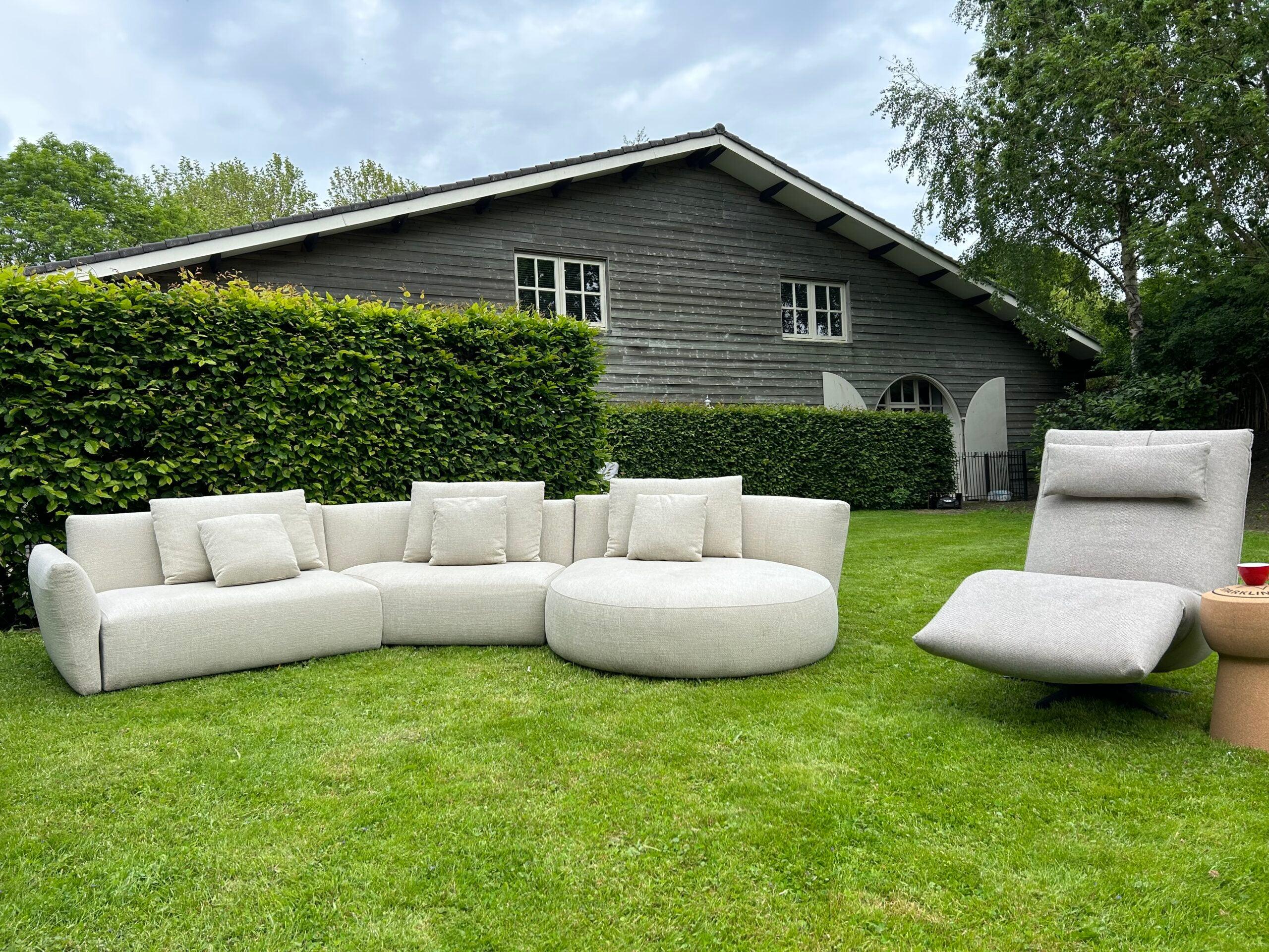 "Stijlvolle buitenlounge set bestaande uit een modulaire hoekbank en ligstoel op een goed onderhouden gazon voor een klassieke houten schuur met groene klimop"