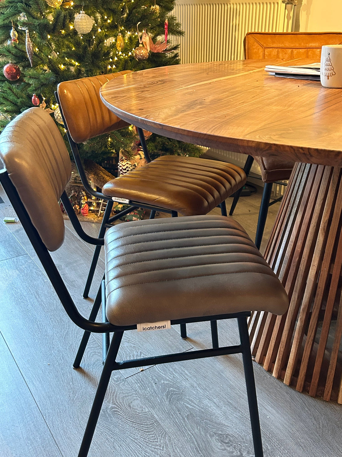 Sfeervolle foto van twee moderne, bruine eetkamerstoelen aan een houten tafel, met een kerstboom op de achtergrond.