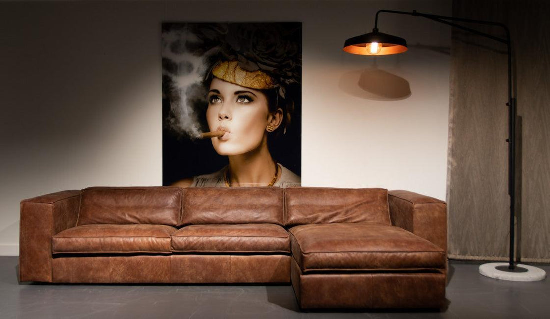 "Stijlvolle bruine leren hoekbank in een minimalistische woonkamer met een groot kunstwerk aan de muur en een industrieel ontworpen staande lamp."