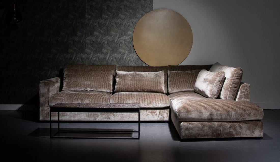 Stijlvolle fluwelen hoekbank met corduroy bekleding en bijzettafel in een minimalistische interieursetting met donkere accentmuur en cirkelvormige kunst op de achtergrond.