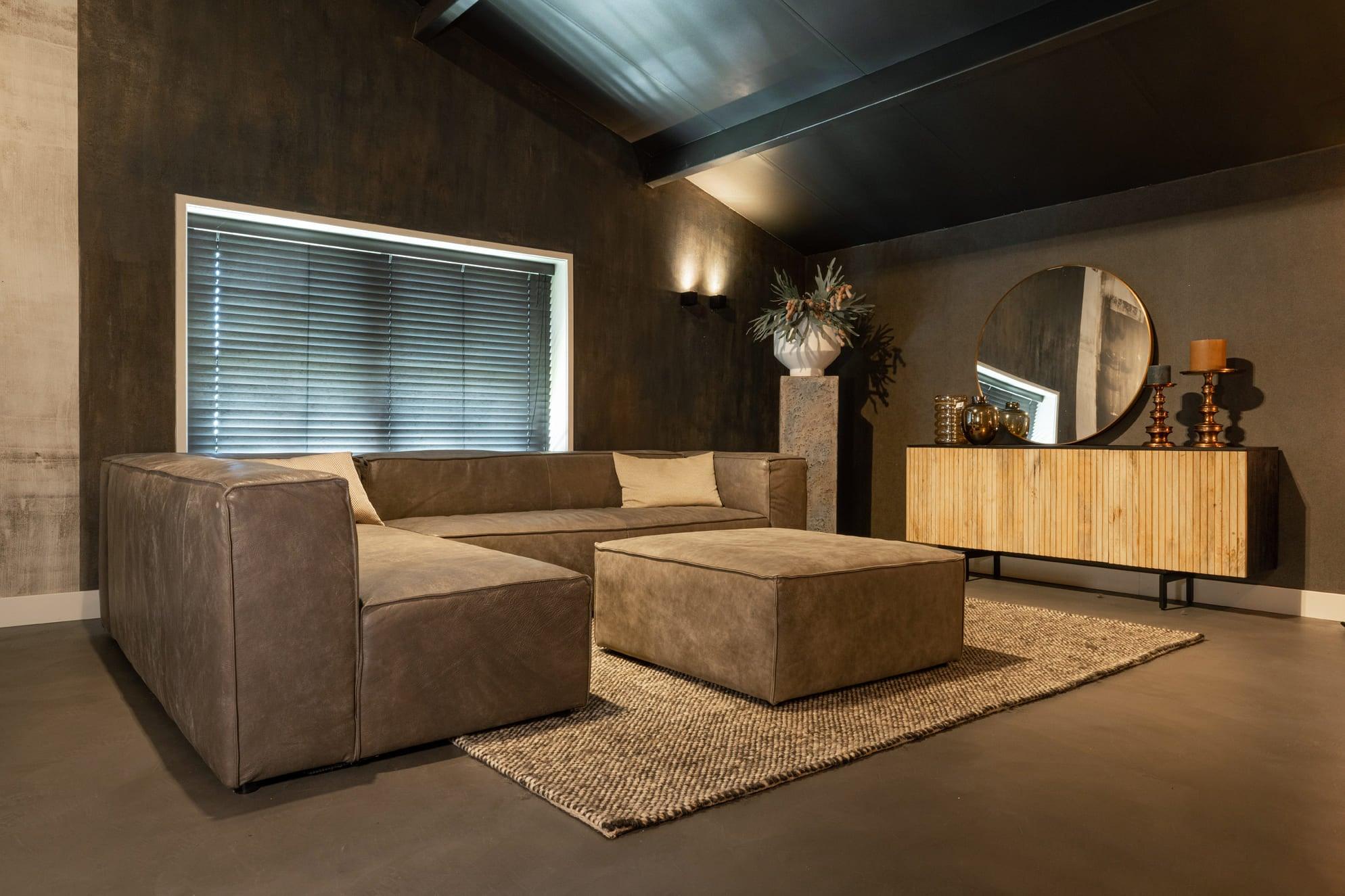 "Moderne woonkamer in industrieel design met een ruime leren hoekbank, visgraat houten sideboard, ronde spiegel, geweven vloerkleed en stijlvolle verlichting."