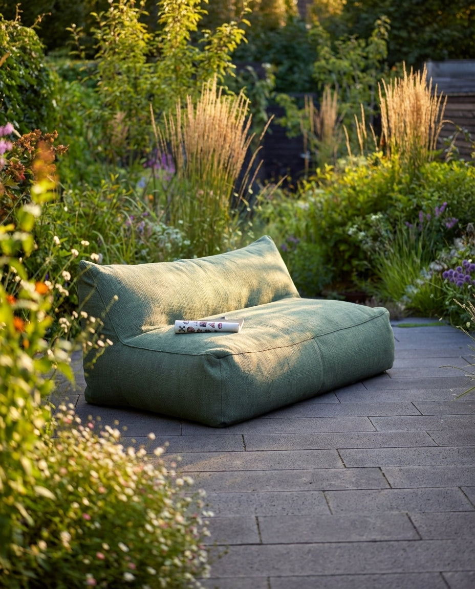 Groene lounge stoel buiten van HoekbankXXL, geplaatst op een stenen terras in een weelderige tuin.
