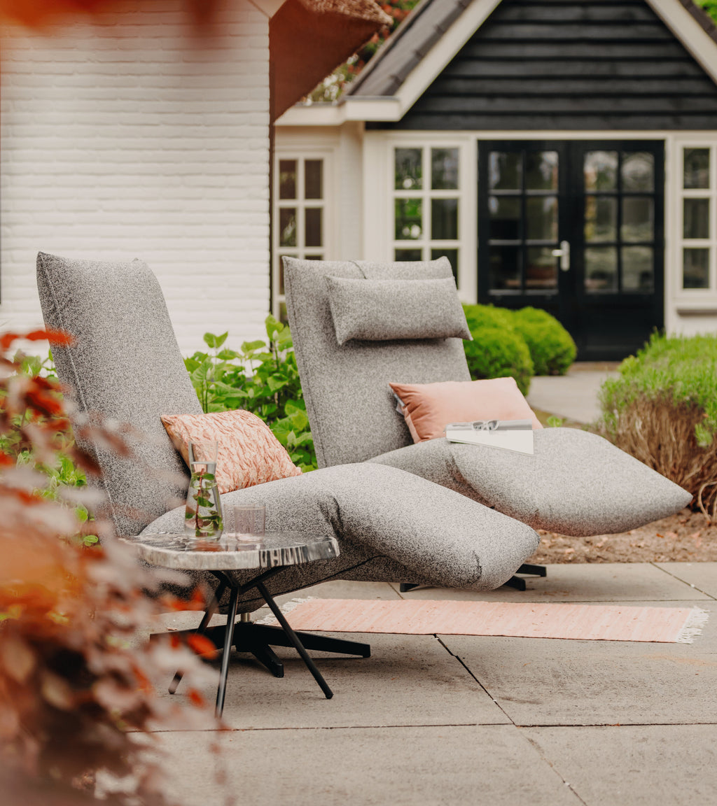 Grijze relax loungestoel buiten van HoekbankXXL, met roze kussens en een bijzettafel op een terras.
