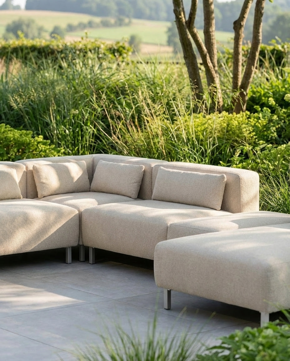 Beige loungebank voor in de tuin, Aruba van HoekbankXXL, op een stenen terras met een groene achtergrond.
