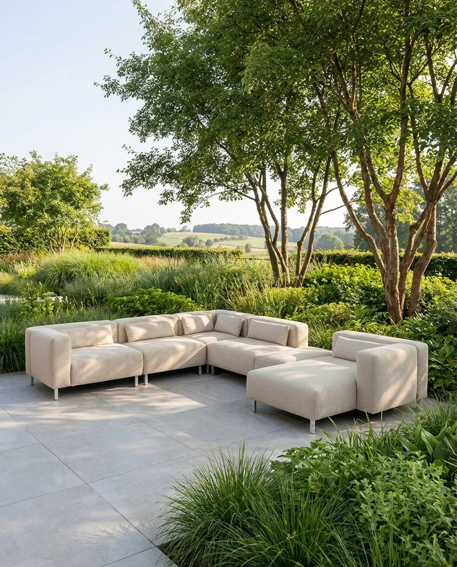 Beige loungebank tuin Aruba van HoekbankXXL, op een terras met groene beplanting en bomen op de achtergrond.
