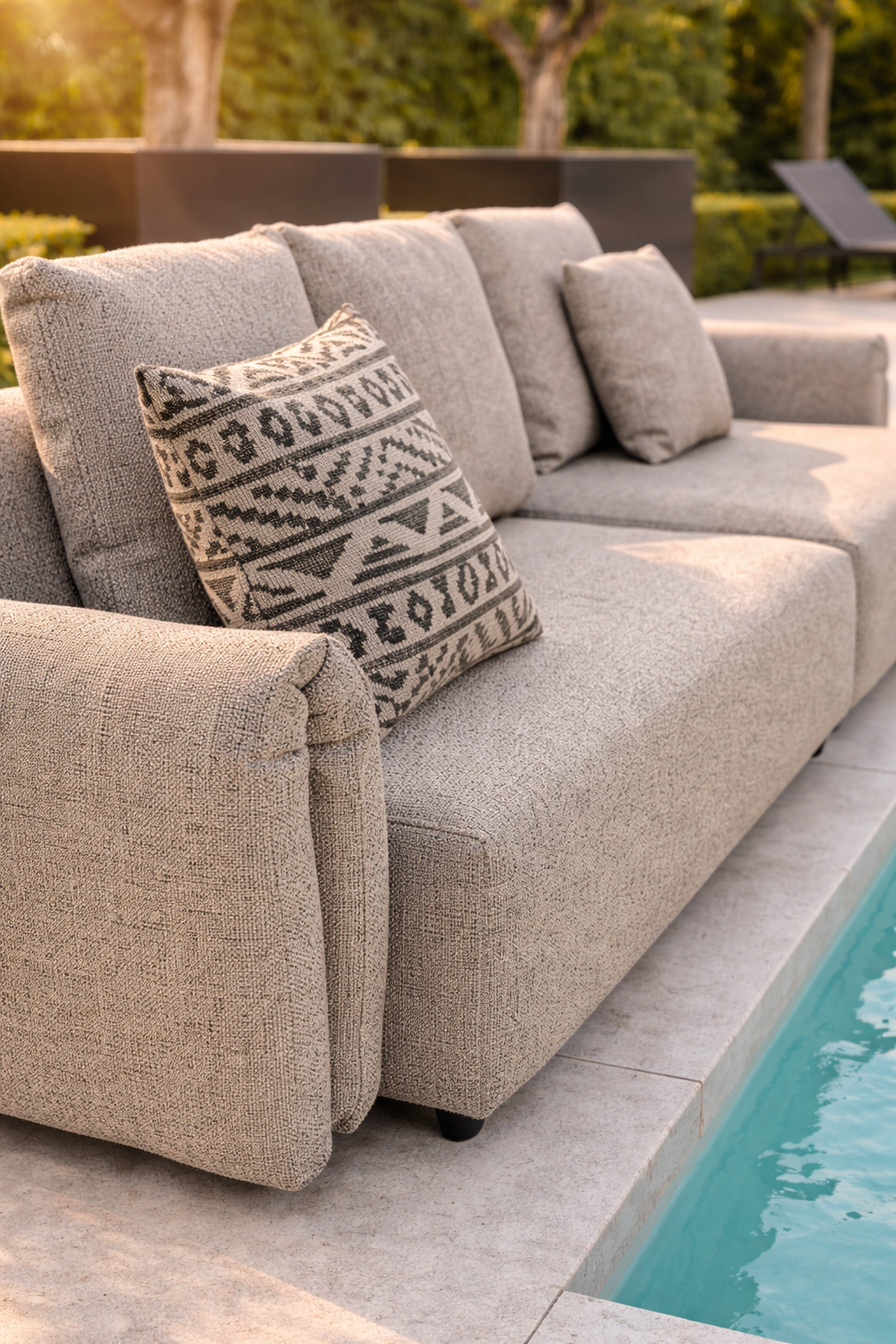 Grijze loungebank tuin van HoekbankXXL, met decoratief kussen met geometrisch patroon, naast een zwembad.
