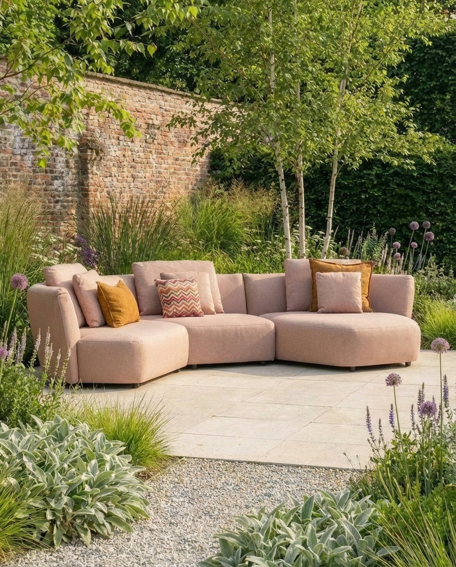 Roze loungebank tuin van HoekbankXXL met diverse kussens in een groene tuin.
