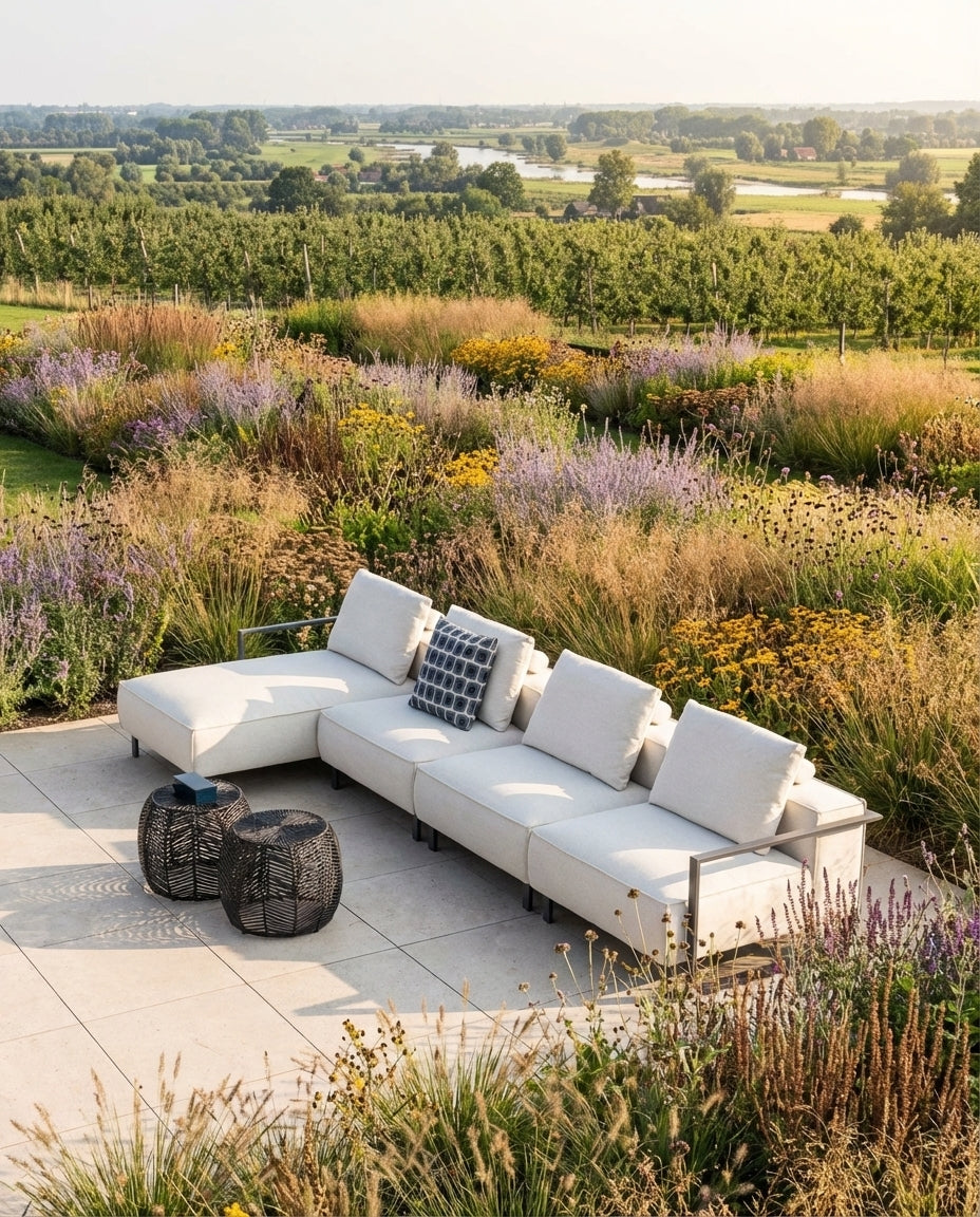 Loungebank tuin wit van HoekbankXXL, met kussens op een terras omringd door bloemen en planten.
