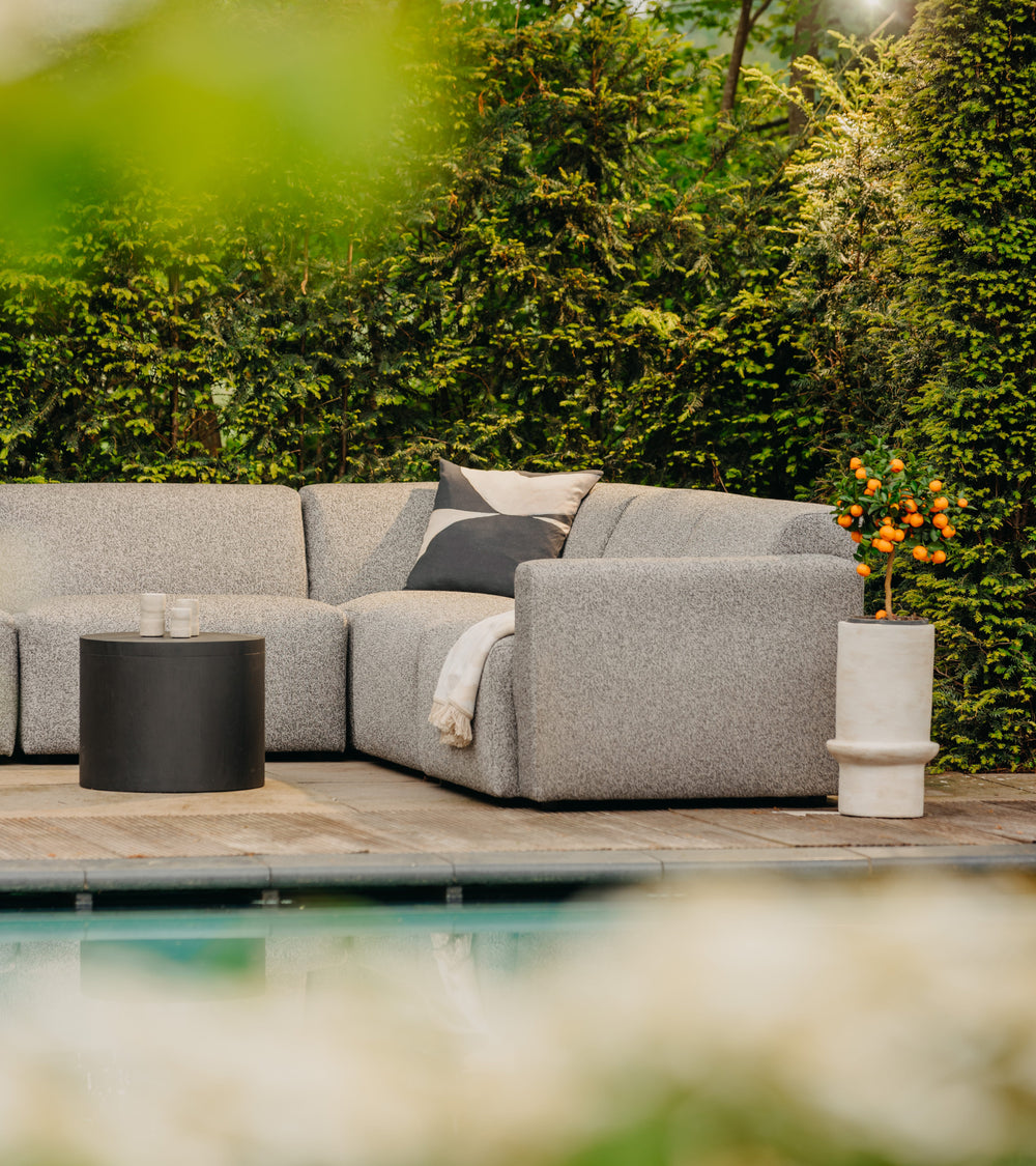 Grijze loungebank tuin van HoekbankXXL met een decoratief kussen en een klein zwart tafeltje buiten bij het zwembad.
