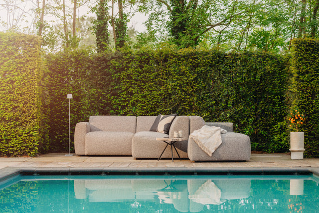 Grijze loungebank tuin van HoekbankXXL met kussens en een bijzettafel, op een terras aan het zwembad.
