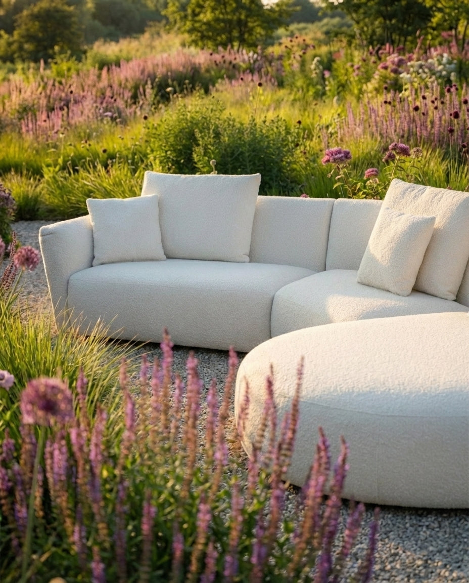 Witte loungebank tuin Salina van HoekbankXXL, met zachte bouclé textuur, in een groene tuin met bloemen.
