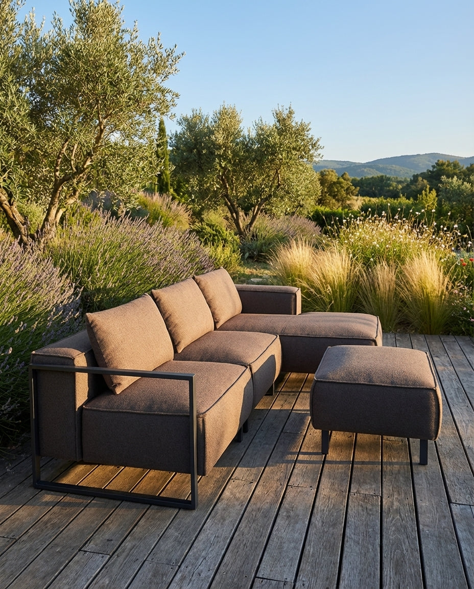 Bruine loungebank tuin - Santorini van HoekbankXXL, geplaatst op een houten terras met een groene tuin op de achtergrond.
