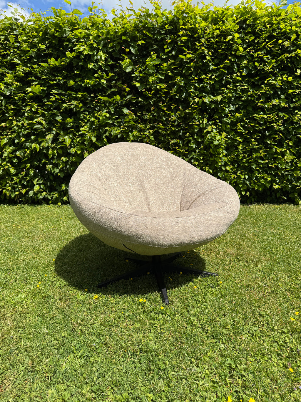 Beige outdoor fauteuil Bora Bora van HoekbankXXL, geplaatst op een groen gazon tegen een groene haag.
