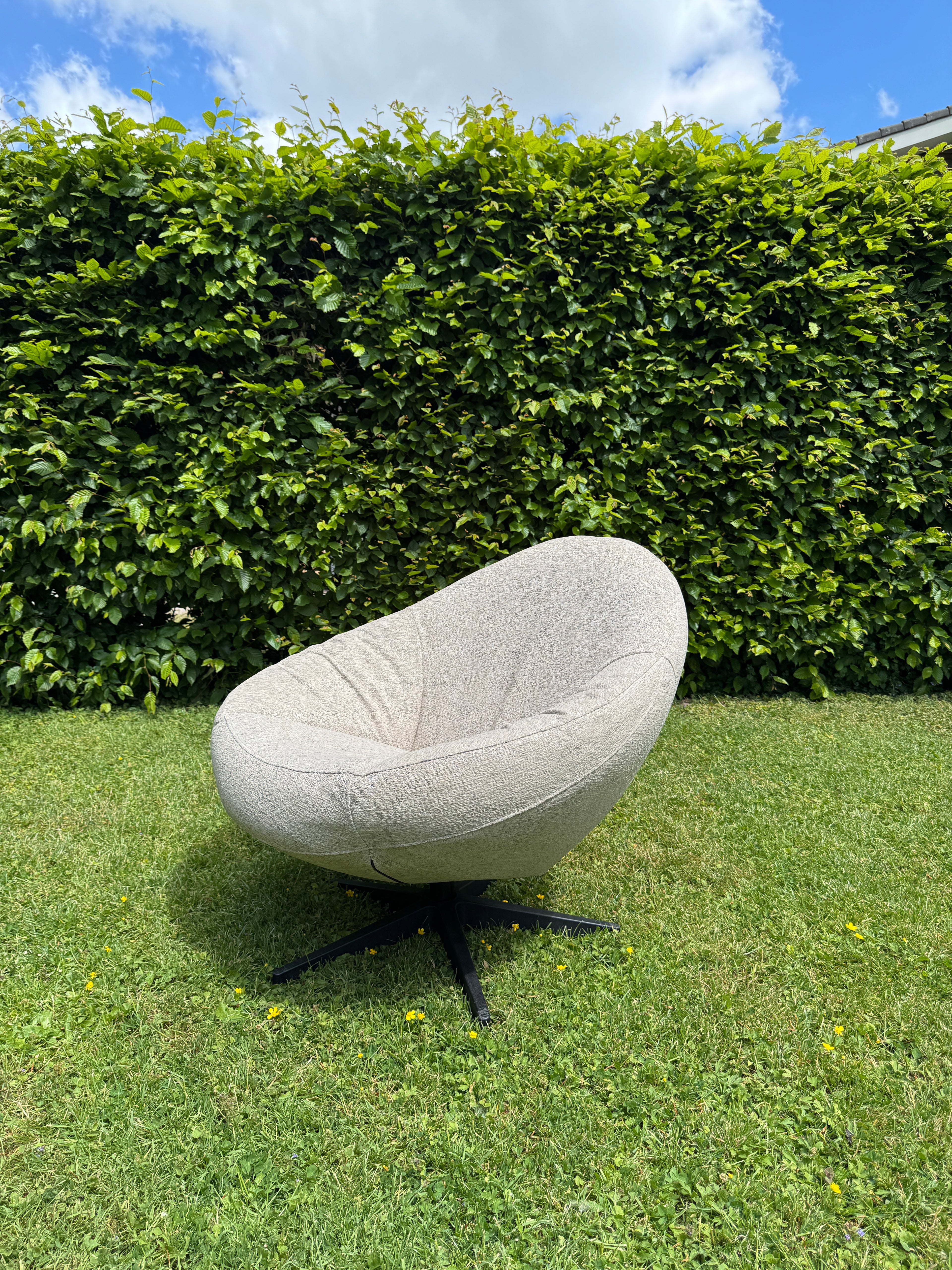 Beige outdoor fauteuil Bora Bora van HoekbankXXL, op groen gras met een groene heg op de achtergrond.
