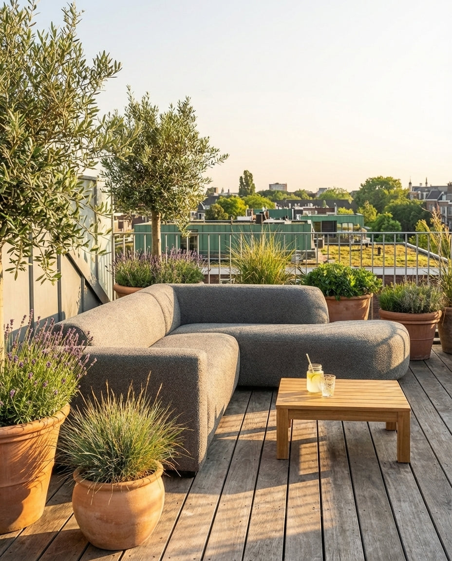 Grijze Penna outdoor loungebank van HoekbankXXL, met houten tafel en diverse planten op een houten terras.
