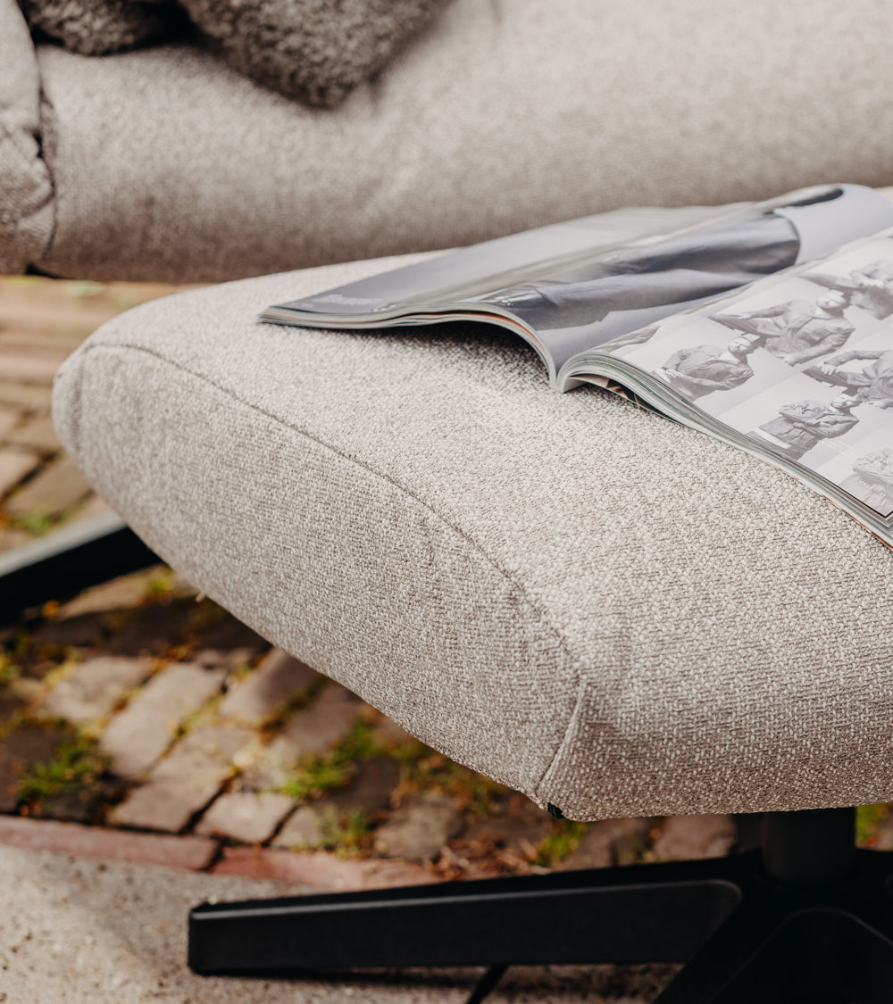 Grijze lounge fauteuil van HoekbankXXL met een open magazine erop, op een betegelde achtergrond.
