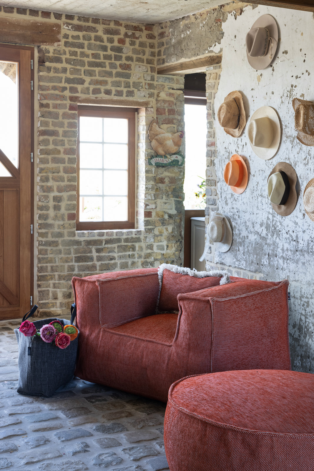 Oranje Silky Clubchair loungestoel van HoekbankXXL, buiten geplaatst op een stenen vloer met een bijpassende poef en een grijze tas met bloemen.
