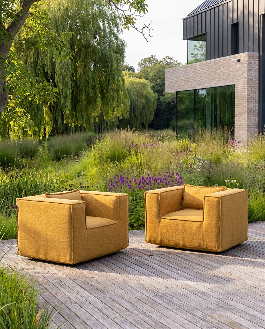 Silky clubfauteuil loungestoel voor buiten van HoekbankXXL, geelkleurige bekleding op houten terras met tuin op de achtergrond.

