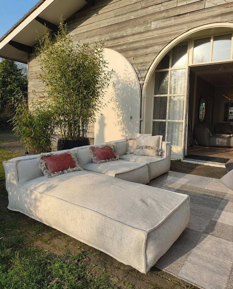 Crèmekleurige Silky Lounge 3-delige set van HoekbankXXL, met rode en beige sierkussens buiten op een patchwork tapijt.
