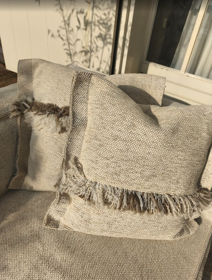 Beige loungebank tuin set van HoekbankXXL met twee sierkussens met franjes op de bank.
